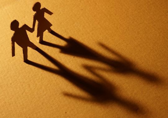 שתי דמויות מקרטון של בן ובת מחזיקים ידיים על רקע חום עם הצל שלהם