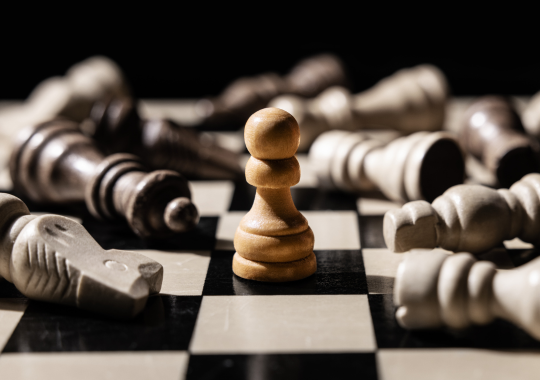 חייל של שחמט בצבע חום בהיר על לוח בצבע שחור ולבן וכל שאר הדמויות במשחק שכובות מסביבו