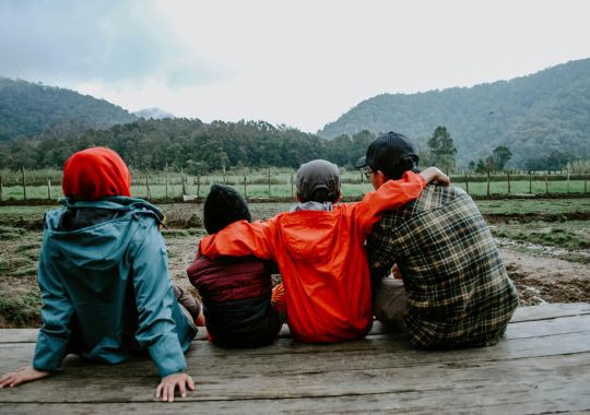משפחה של שני הורים ושני ילדים יושבים על דק ברקע עצים והרים
