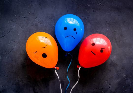 בלונים בצבעים אדום, כחול וכתום עם פרצופים עליהם ברקע אפור