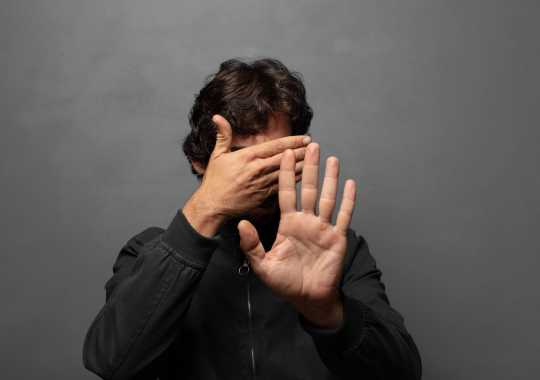 בחור עם חולצה שחורה שם יד אחת לכסות את הפנים ואת היד השניה כמו תמרור עצור מקדימה