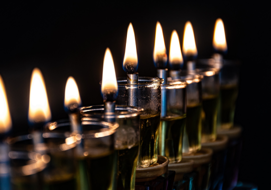 כוסות שמש מלאות בשמן זית על חנוכיה שדולקים ממנה פתילות באש