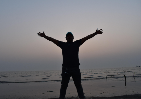 צללית של אדם עומד עם שתי ידיים פרוסות לצדדים וברקע יש את הים בשעות הערב המוקדמות