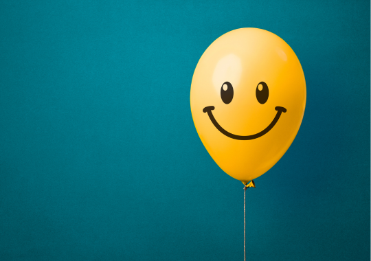 בלון צהוב עם ציור של סמיילי עליו ברקע כחול טורקיז